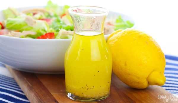 lemon olive oil dressing in a glass karafe in front of a big white bowl of salad