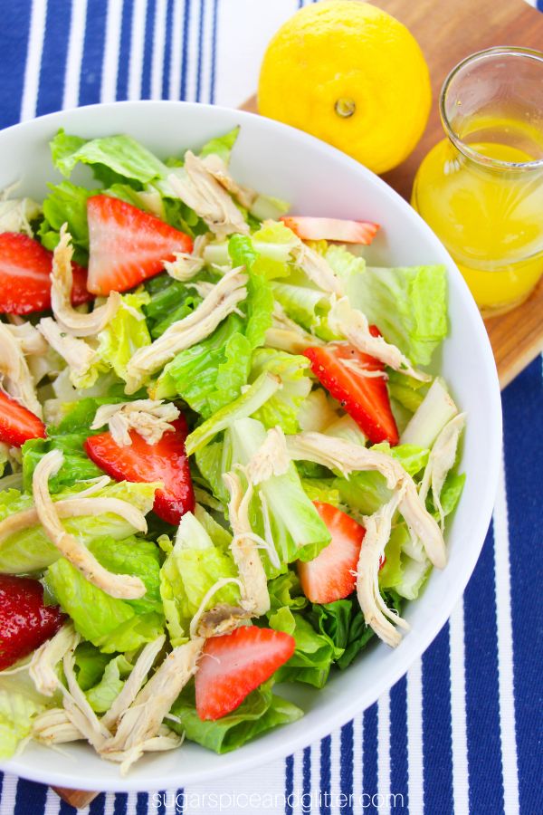 overhead picture of a chicken and strawberry salad on a striped blue placemat with lemon salad dressing in the background
