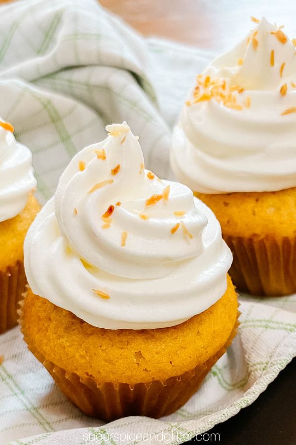 close-up picture of a coconut lime cupcake topped with toasted coconut shreds, sitting on top of a green and white plaid napkin