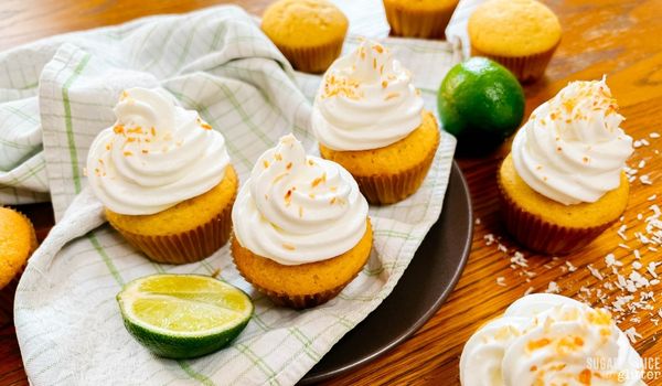 a black plate topped with a green plaid napkin and three coconut lime cupcakes, surrounded by cupcakes in various stages in completion