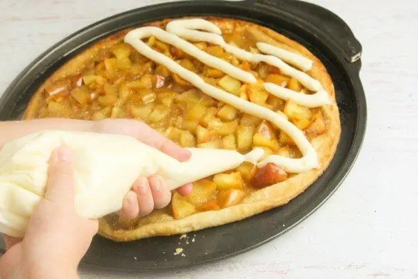 Apply a generous amount of cream cheese frosting to your apple pie pizza with a piping bag
