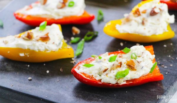 Close-up image of baby bell peppers stuffed with cream cheese and topped with pecans and green onions on top of a slate tray
