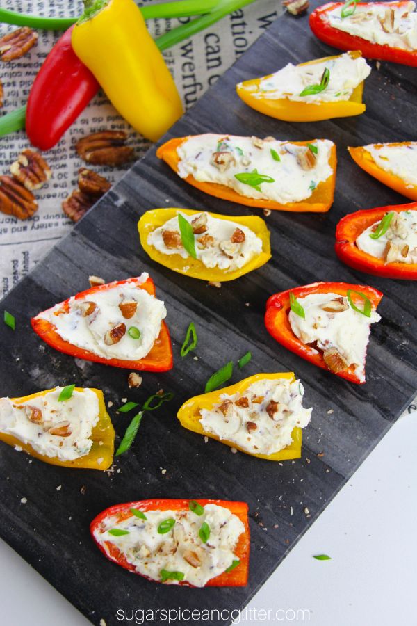 Overhead image of baby bell peppers stuffed with cream cheese and topped with pecans and green onions on top of a slate tray