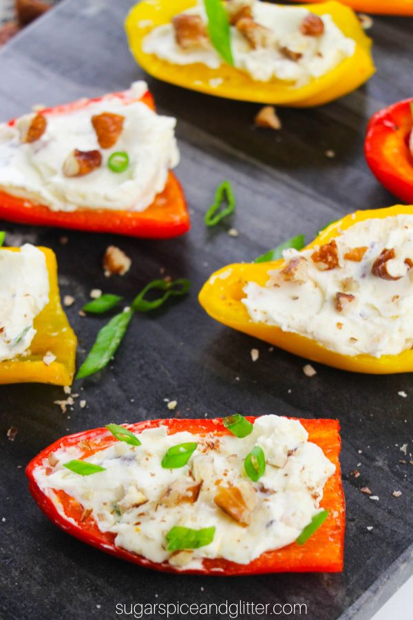 Baby bell peppers stuffed with cream cheese and topped with pecans and green onions on top of a slate tray