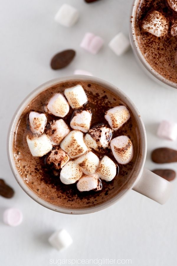 overhead image of a mug of spiked hot cocoa with marshmallows sprinkled around it