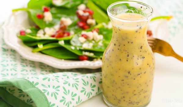 close-up picture of a karafe of orange poppy seed salad dressing with a spinach salad in the background