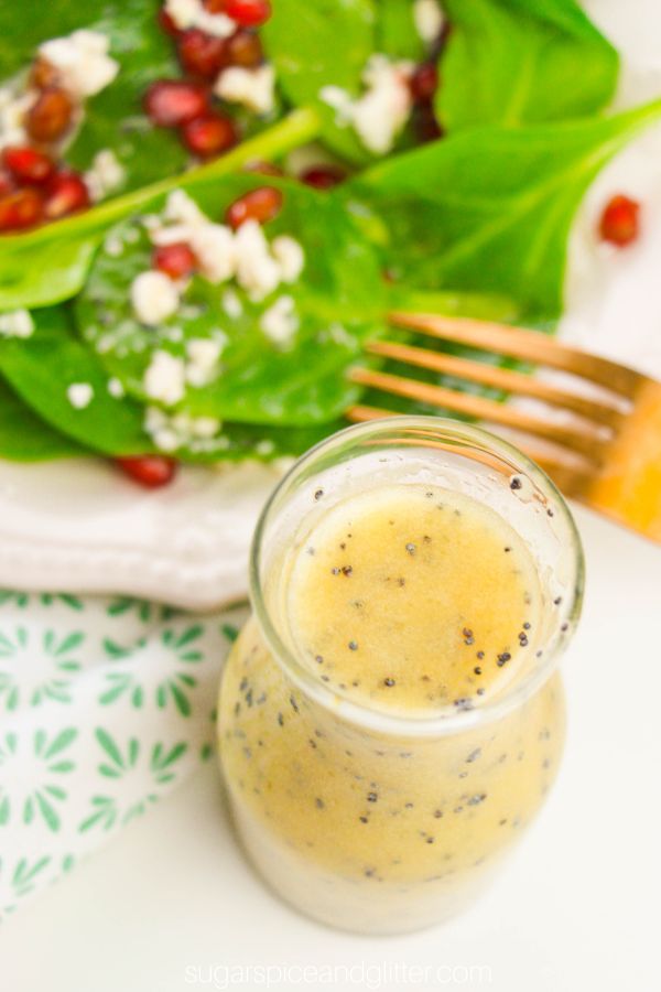 overhead picture of a karafe of orange poppy seed salad dressing with a spinach salad in the background