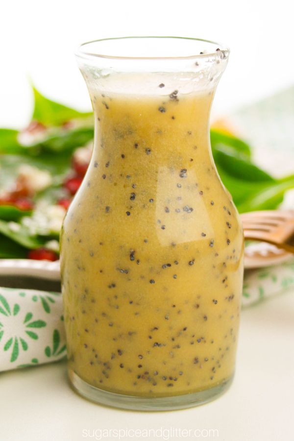 close-up picture of a karafe of orange poppy seed salad dressing with a spinach salad in the background