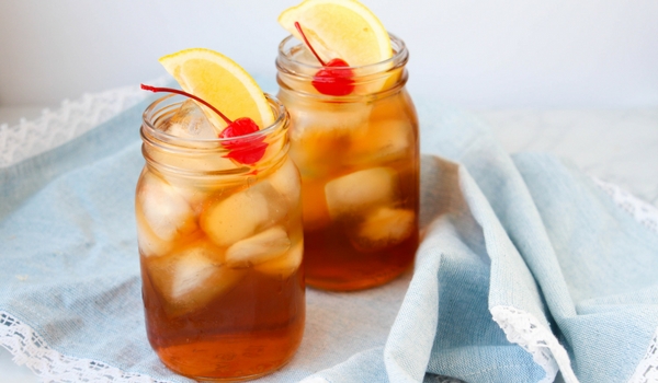 two mason jars full of Long Island Iced Tea garnished with lemon wedges and maraschino cherries on a denim napkin
