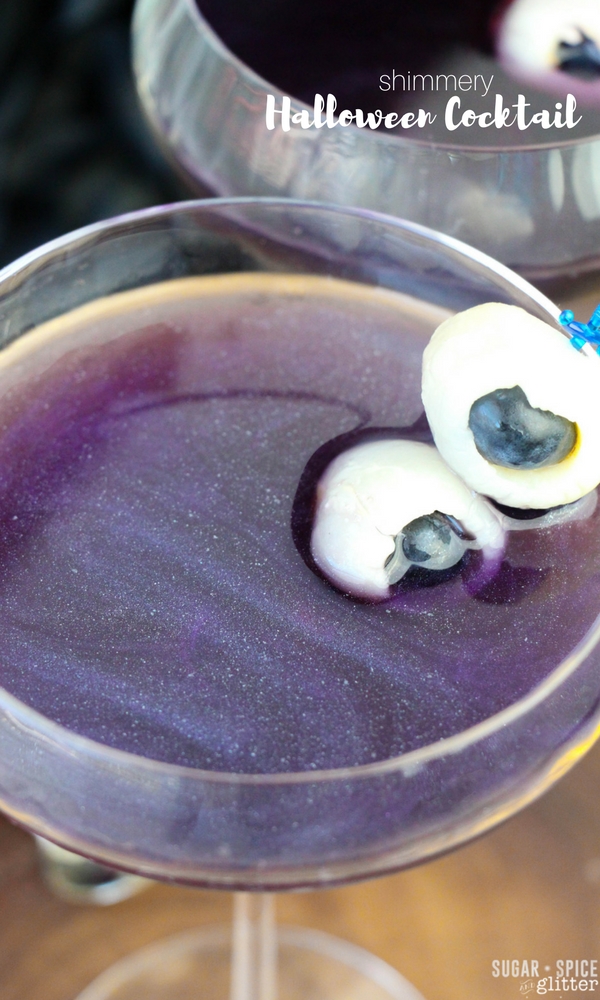 A shimmery and sparkly rum cocktail that looks like a purple night sky with edible eyeballs skewered for a Halloween touch