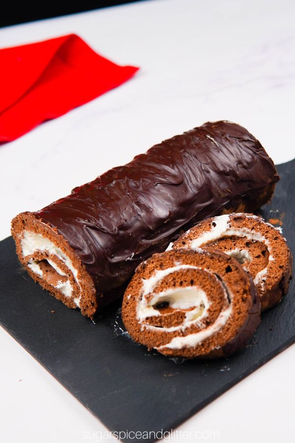 overhead shot of chocolate roll cake with two slices placed in front of the roll, on top of a black cutting board