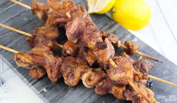 sumac chicken kebabs on a slate gray tray with lemons on the side