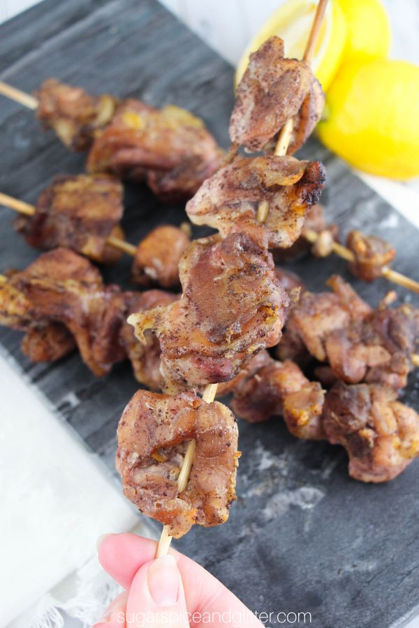 hand holding up a sumac chicken kebab over a gray tray holding more kebabs