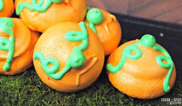 orange pumpkin meringue cookies with green piped vines and stem on a bed of grass