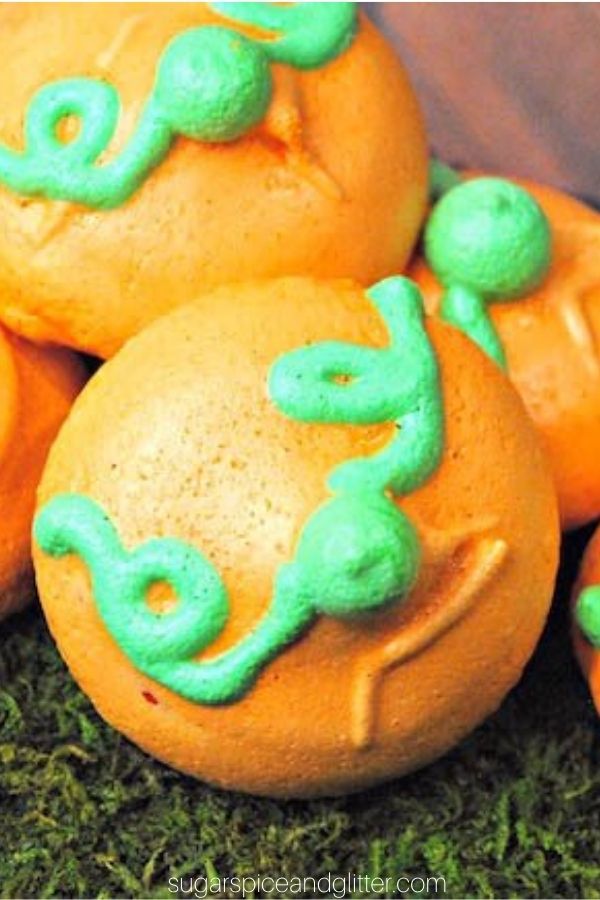close-up image of orange pumpkin meringue cookies with green piped vines and stem on a bed of grass