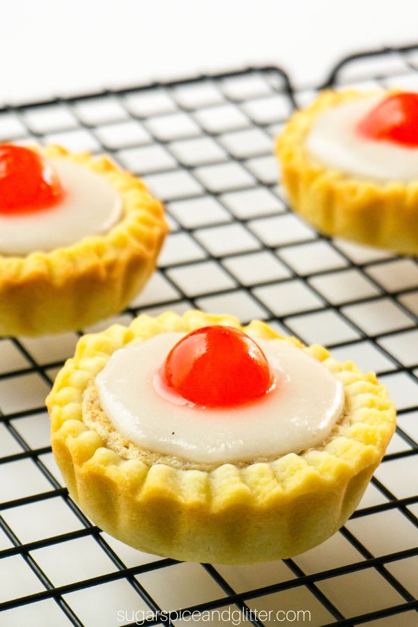 Two-bite pie tarts with a bright red cherry on top set on a cooling rack