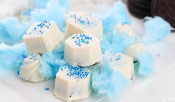 picture of a pile of white truffles with blue sprinkles on a bed of blue cotton candy with OREOs in the background