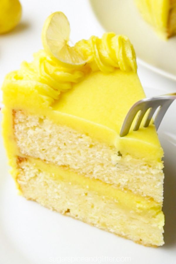 A slice of lemon cake on a white plate with a fork just inserted into the top of the cake's frosting, about to dig in for a bite