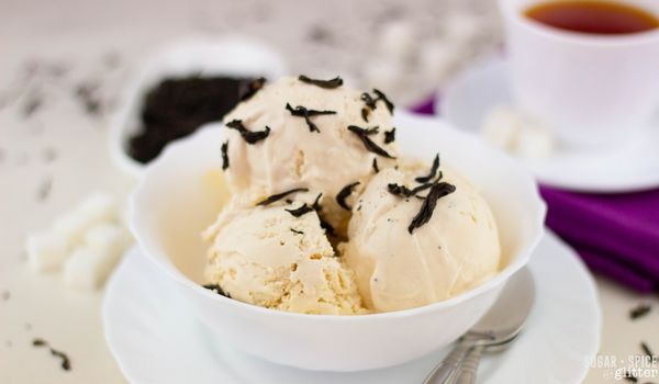 white bowl of London Fog ice cream with tea leaves scattered on top, a cup of tea in the background and various tea accoutrements scattered around