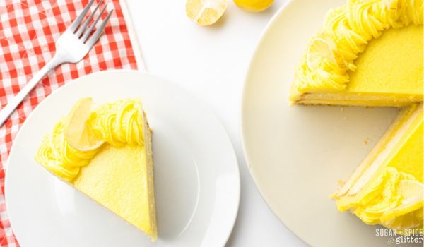 Overhead shot of a lemon cake and a slice of lemon cake, both on white plates with a red plaid napkin underneath