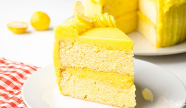 A slice of lemon cake on a white plate with a sliced lemon in the background