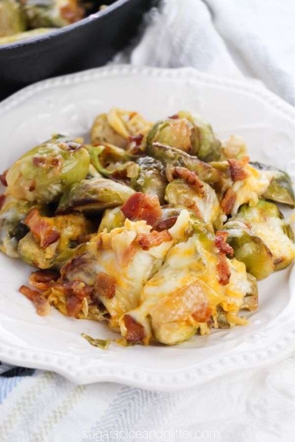 Cheese and bacon covered brussels sprouts on a white plate set against a blue striped napkin
