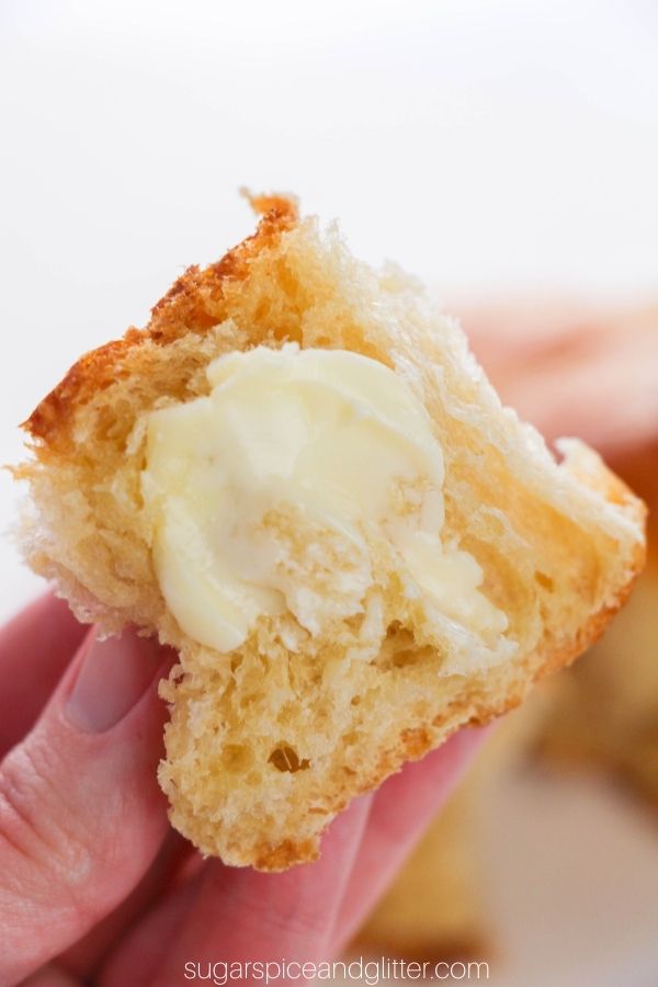 a hand holding a sliced Hawaiian dinner roll smeared with butter