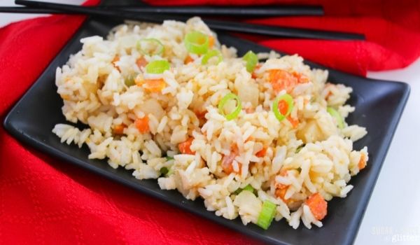 black square dish piled high with fried rice on a red napkin with black chopsticks in the background