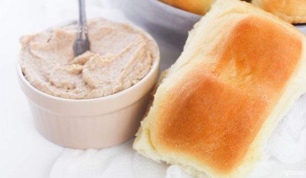 close-up image of a bread roll alongside a jar of cinnamon honey butter