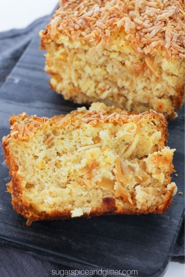 two slices of of pineapple coconut loaf on a slate gray tray with the full loaf in the background