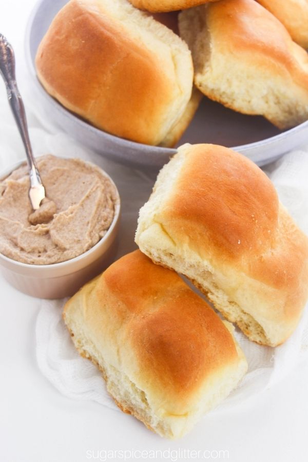 overhead image of two Texas Roadhouse-style bread rolls alongside a jar of cinnamon honey butter in front of a bowl holding more rolls