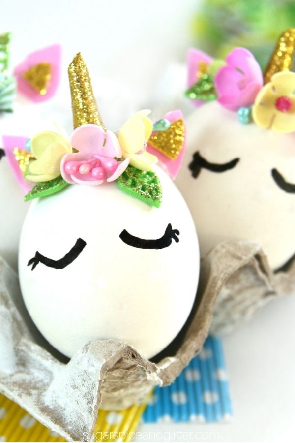 close-up shot of an Easter Egg decorated with a unicorn horn, ears and a flower crown set inside an egg carton with more unicorn Easter eggs in the background