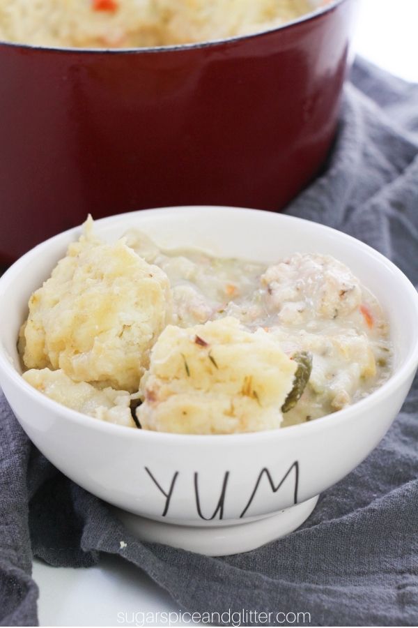 a white bowl with YUM written on it filled with chicken and dumpling stew on a gray napkin