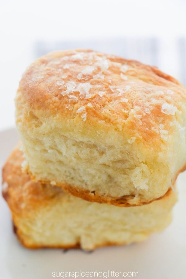 two stacked buttermilk biscuits with flaked sea salt on top, set on a white plate