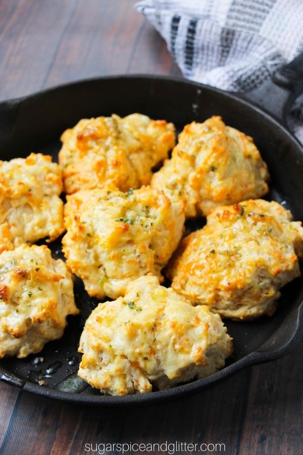 cast-iron pan full of buttery cheddar bay biscuits on a wooden table, a striped towel wrapped around the pan handle