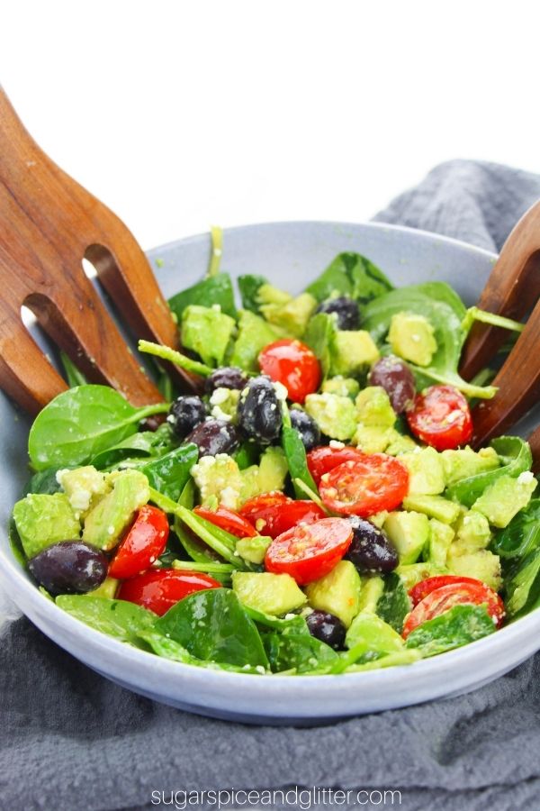 a large blue bowl full of Greek spinach salad with wooden salad hands digging in