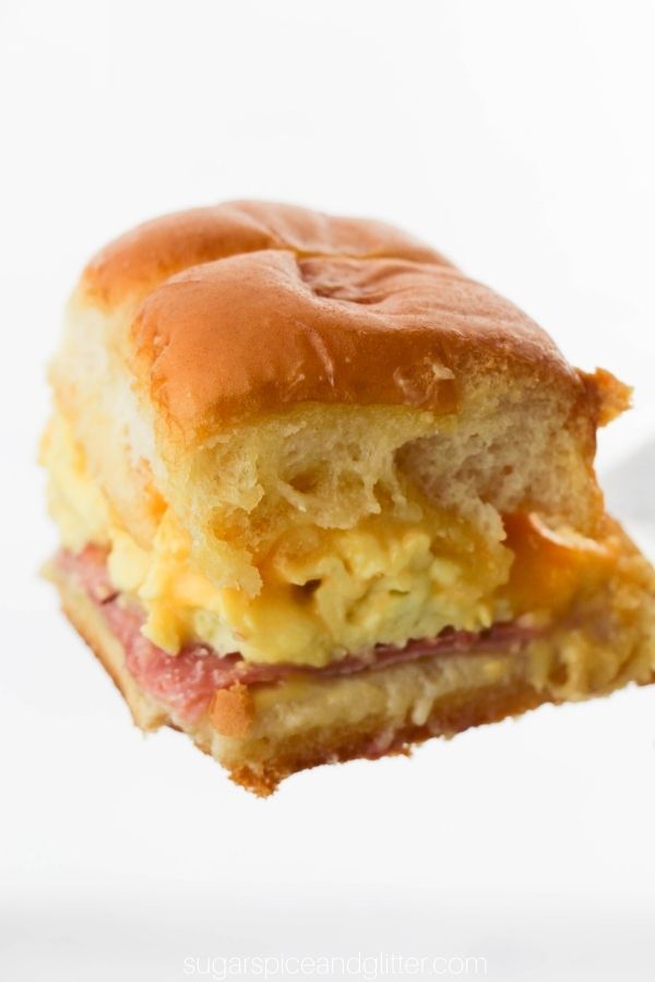golden breakfast slider with melted cheese and fluffy eggs being held against a white background by a silver spatula