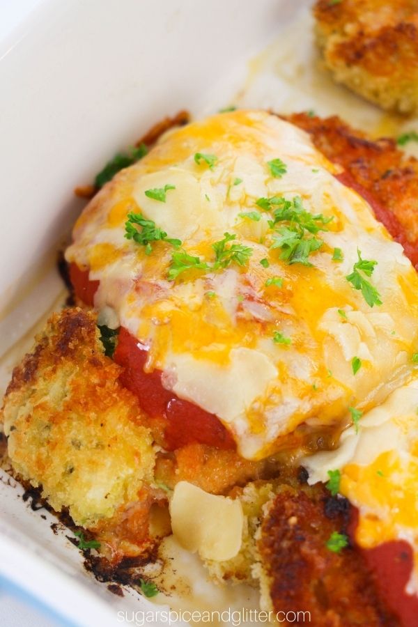 close-up image of chicken parmesan with melted cheese and a garnish of parsley in a white casserole dish