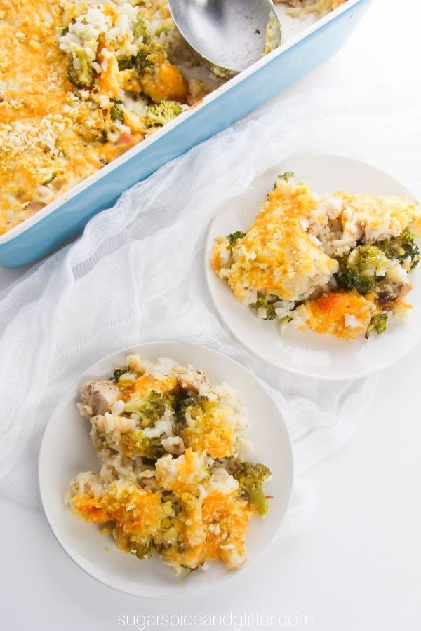 overhead image of two small white plates filled with broccoli chicken casserole topped with cheese and bread crumbs along with the casserole dish with the remaining casserole
