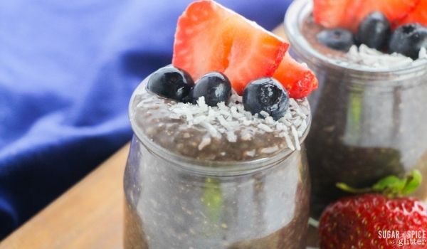 close-up image of a yogurt glass jar filled with chocolate chia seed pudding topped with strawberries, blueberries and shredded coconut