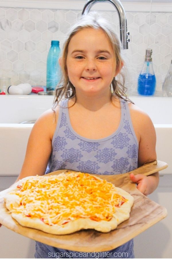 child holding a pizza peel with an uncooked pizza on the peel, ready to go in the oven