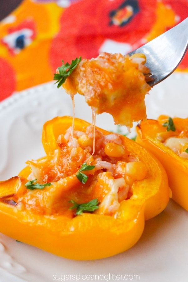 close-up shot of a taco-stuffed yellow bell pepper on a white plate, sprinkled with cilantro, a fork pulling a cheesy bite out of the pepper