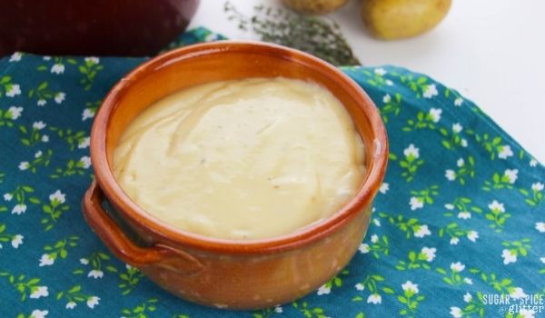 brown clay bowl filled with potato leek soup with more ingredients in the background