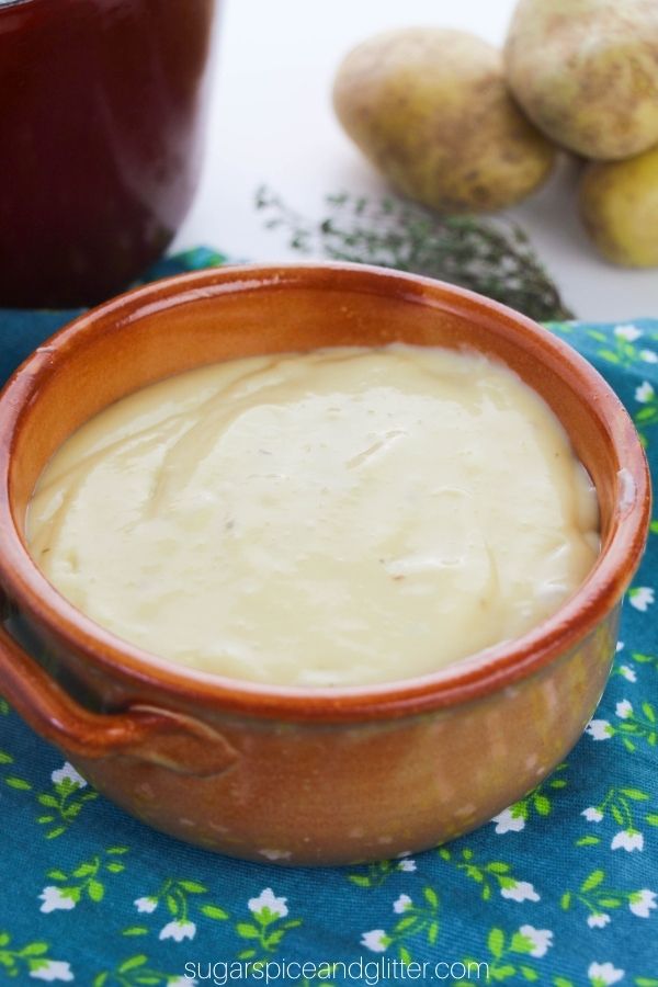 brown clay bowl filled with potato leek soup with more ingredients in the background