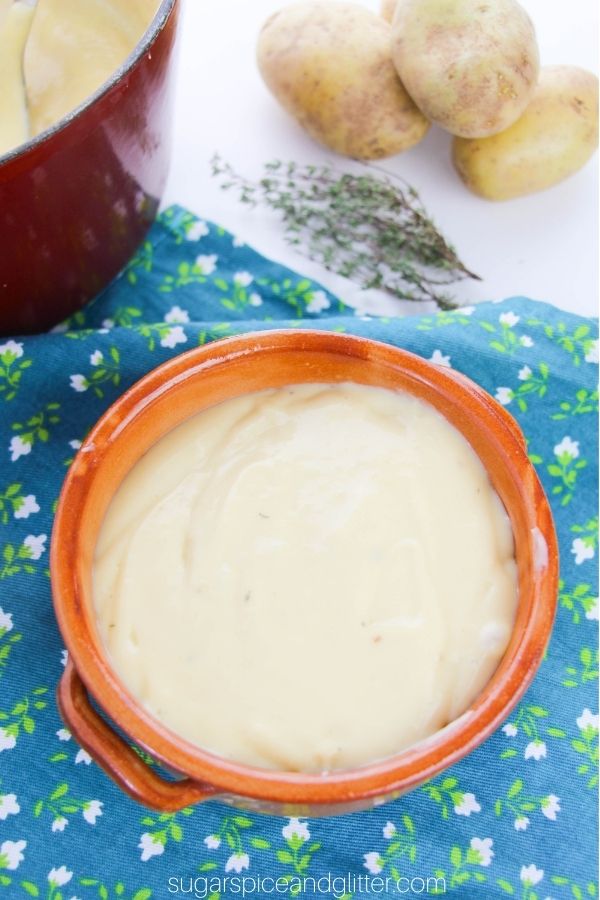 overhead image of a brown clay bowl filled with potato leek soup with more ingredients in the background