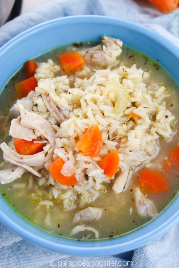 overhead picture of a blue bowl filled with chicken and rice soup with bright pops of orange from the carrots in the recipe