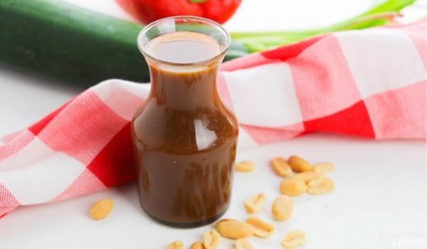 a small glass karafe filled with homemade Kung Pao sauce surrounded by a scattering of peanuts
