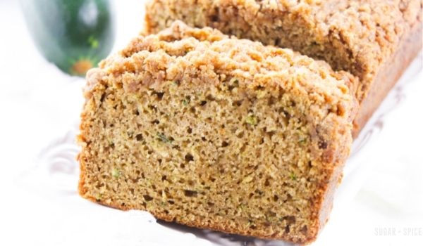 slices of zucchini coffee cake on a white platter with fresh zucchini in the background
