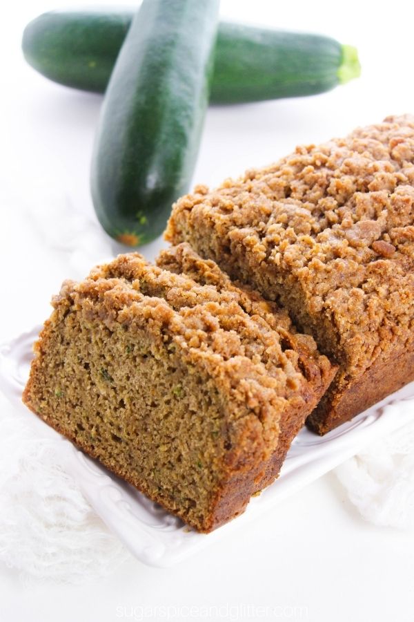 slices of zucchini coffee cake on a white platter with fresh zucchini in the background