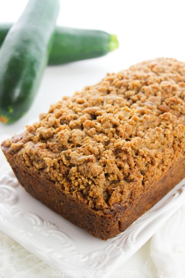 zucchini coffee cake on a white platter with fresh zucchini in the background